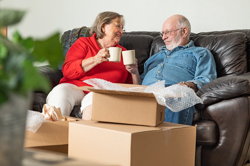 Senior couple sitting on the couch with coffee surrounded by boxes